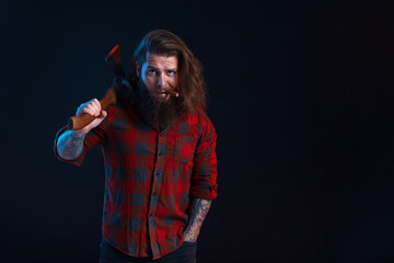 Emotional man with cigar holds old axe. Bearded lumberjack in checkered shirt with long hair