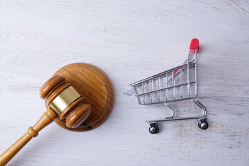 grocery cart and judge gavel on white brick wall background