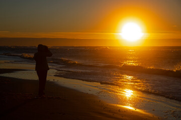 Silhouette of a young woman at the beach enjoying sunset - obrazy, fototapety, plakaty