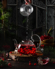 Healthy hot drink with red berries viburnum, pouring hot water from glass into teapot . Bubbling tea. Christmas drinks. 