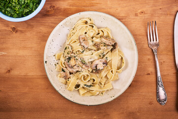 Portion of classic italian pasta in a plate - fettuccine with mushroom creamy sauce and bowl with parsley on the table, top view