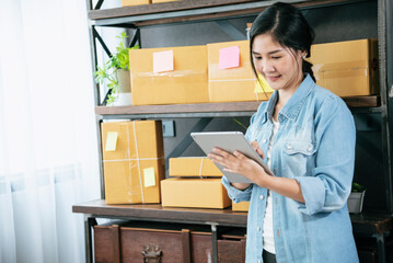 Asian woman startup small business at home office. Online seller entrepreneur young asian woman use tablet checking online order. Woman using tablet check stock goods supply delivery package shipping