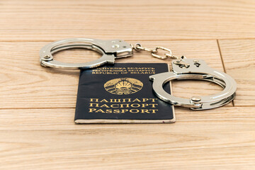 Passport of a citizen of the Republic of Belarus and steel handcuffs on a wooden background. Blurred background. Close-up.