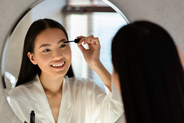 Beautiful chinese lady applying makeup in bathroom
