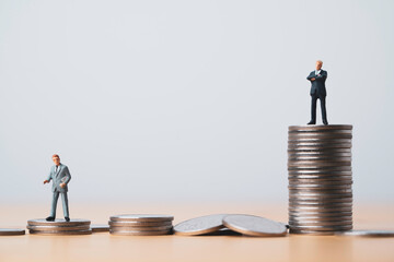 Miniature figure of two businessmen standing to different high and low coins stacking for position...