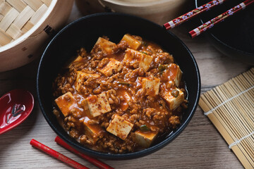 Black bowl with chinese traditional mapo tofu over brown wooden background, middle close-up, studio shot
