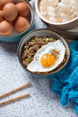 Bowl of fried rice and mince topped with a fried egg, studio shot on a beige granite background, elevated view