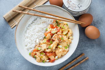 Plate with chinese tomato egg-stir fry and white rice, high angle view on a light-blue stone background, horizontal shot
