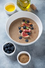 Flaxseed porridge served with blueberry, sliced figs and almonds in a white bowl, vertical shot on a light-blue stone surface
