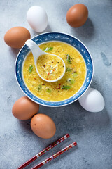Egg-drop soup or chinese soup of wispy beaten eggs in chicken broth, vertical shot on a light-blue stone background