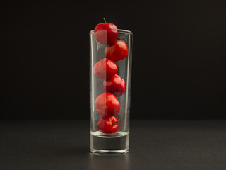 Ripe red acerola cherries in glass on a cement floor with a black wall background
