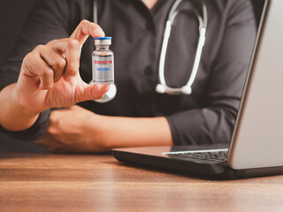 Hand of a doctor holding a COVID-19 vaccine bottle while sitting in the hospital or clinic