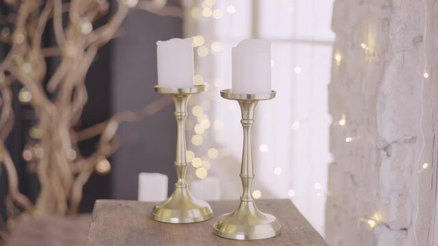 Beautifully decorated holiday interior. Close-up view 4k stock video footage of two candles standing on wooden background. Christmas, wedding or Valentines day celebrations romantic decor