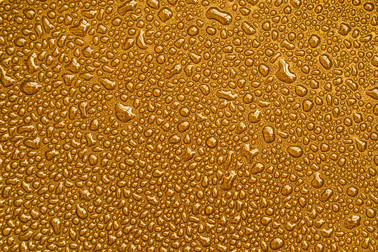 Drops, drips, blobs, beads, dribbles of water on the gold brilliant surface. Monochrome macro or closeup background or texture