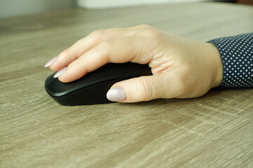 Caucasian Woman using a black wireless computer mouse on white background. A woman's hand holds a...