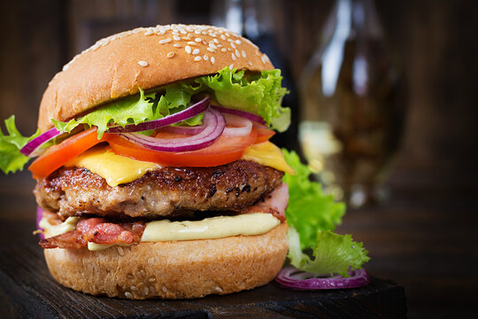 Hamburger with bacon, turkey burger meat, cheese, tomato and lettuce on wooden background. Tasty burger. Close up