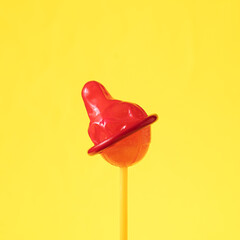 Lollipop with red condom against yellow background.