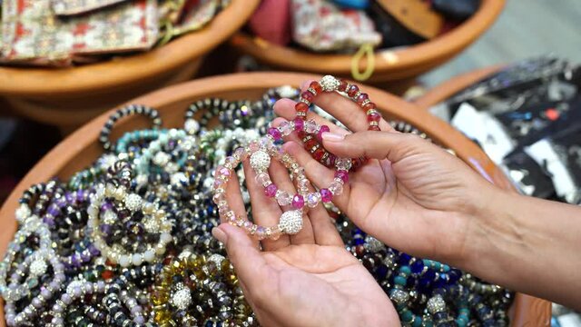 Close-up view 4k stock video footage of woman choosing new shiny and glossy cheap  bracelets in market