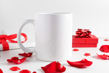 White mug mockup on wooden table with gifts and red rose petals front view. Empty template with copy space for design and logo.