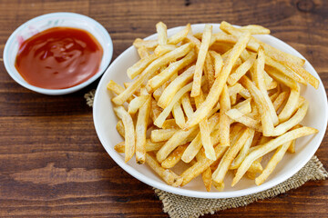 Potato sticks close up in white dish and chilli sauce on an wooden table, snack food