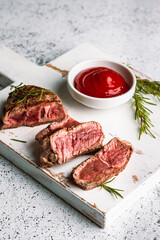 Juicy slices of Rib Eye beef steak on a wooden board with rosemary and tomato sauce