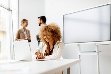 Young businesswoman using laptop in the office with young people works behind her