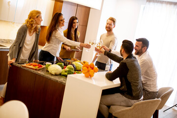 Group of young people preparing meal, drinking white wine and having a good time