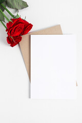 Invitation mockup, greeting card with white sheet of paper on wooden table top view. List template with red roses flat lay.