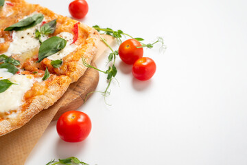 Close-up of a delicious Roman pizza with vegetables on a white background. ripe red tomatoes and micro-greens lie nearby. Traditional Italian food. Side view
