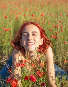 fröhliches Mädchen mit roten Haaren im Mohnfeld