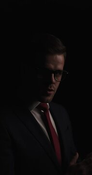 attractive bearded businessman with eyeglasses in a vertical project video being mysterious, adjusting tie, smiling and disappearing in the dark
