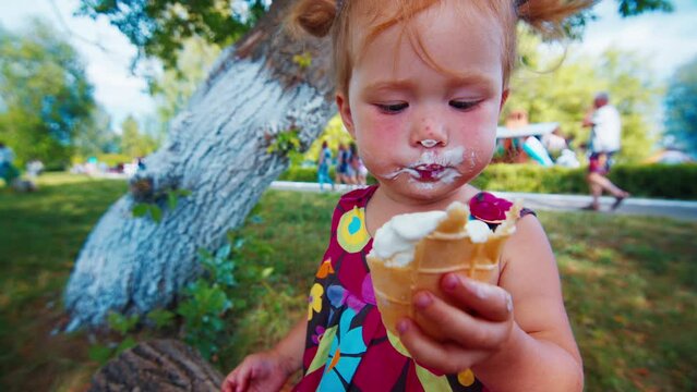 Portrait of the toddler girl with smeared face eating ice cream outdoor