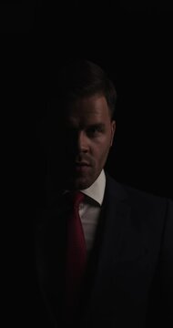 vertical project video of elegant young businessman arranging tie, hair and suit, moving in a back view position and walking away in the dark