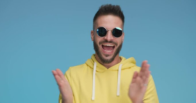 sexy casual man feeling excited, clapping his hands, wearing sunglasses and gesturing good job
