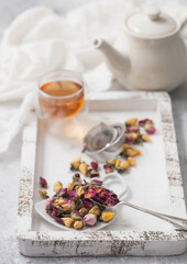 Rose buds mix tea with tea ball strainer infuser and teapot on white background with linen cloth and glass cup