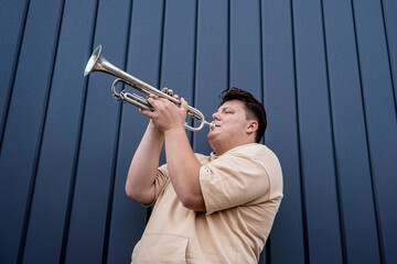 Young street musician playing the trumpet near the big blue wall © romaset