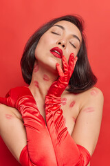 Vertical shot of beautiful thoughtful Asian woman keeps eyes closed wears long red gloves has well...