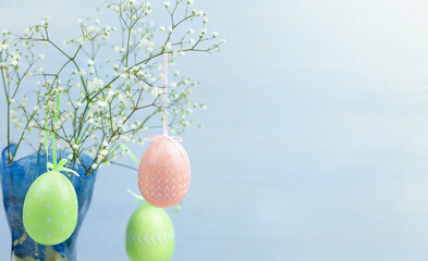 Pink and green Easter eggs hang on flowering branches. Light blue background in the background. Easter decor