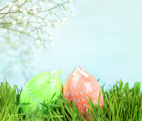 Green and pink Easter eggs in the grass against the blue sky under the branch of a spring flowering tree