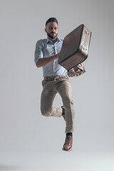 cool young fashion model leaping up while holding jacket and briefcase