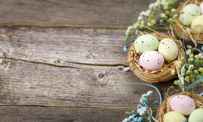 Baskets with Easter colored eggs on a rustic wooden antique table surrounded by delicate spring flowers