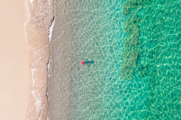 Top view. Young beautiful woman in red hat standing and sunbathe in sea water. Drone, copter photo. Summer vacation. View from above.