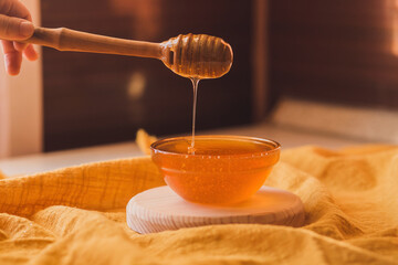 Honey dripping from honey dipper in bowl. Close-up. Healthy organic Thick honey dipping from the...