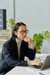 Vertical portrait of young Asian businessman using laptop while working in modern office