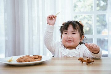 Happy Asian cute girl looks fresh and bright while eat snack and cereal breakfast with toy plane in the morning. Concept of emotional intelligence and child food health care