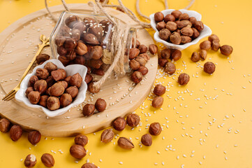Peeled hazelnuts in a bowl and also scattered on a yellow background