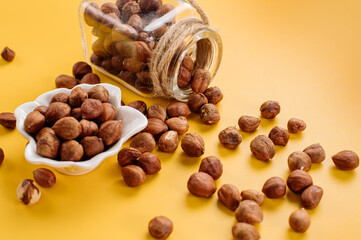 Peeled hazelnuts in a bowl and also scattered on a yellow background