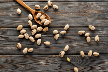 Pistachio nuts are randomly scattered with various accessories on a wooden background