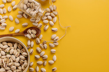 Pistachio nuts are randomly scattered with various accessories on a yellow background
