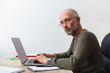 Elderly man working on laptop and looking at camera